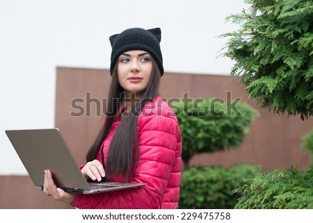 girl in a pink jacket holding a laptop and looking away