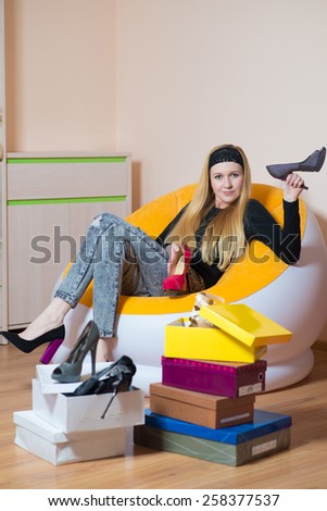 Young pretty woman sitting on a chair and holding women\'s shoes. Woman on the shopping