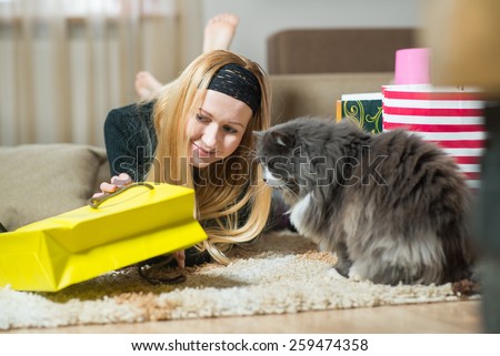 Pretty young woman with cat looking into the bag from store at home. Woman came home from the shopping