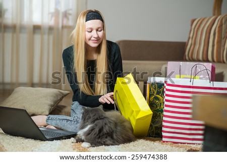 Pretty young woman with cat looking into the bag from store at home. Woman came home from the shopping