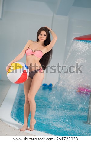 Young pretty woman standing in swimming pool and holding a ball