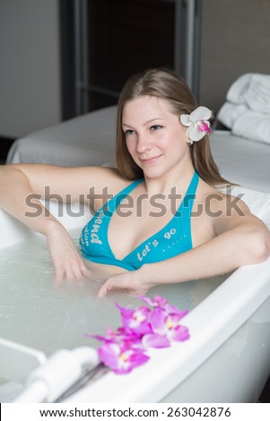 Young pretty woman with flower in the hair taking a bath at the hotel spa
