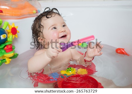 baby sitting in water in a bath and playing with toys. Close portrait