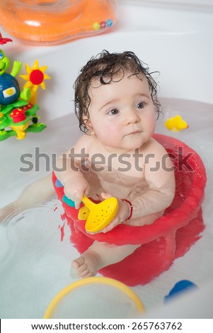 baby sitting in water in a bath and playing with toys. Close portrait