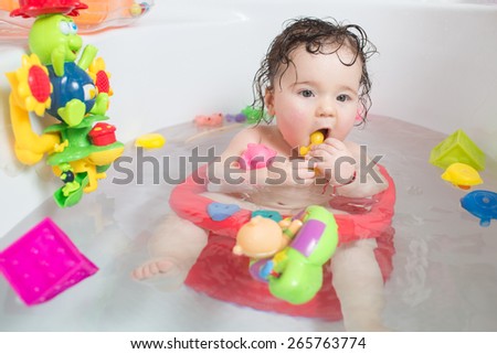 baby sitting in water in a bath and playing with toys. Close portrait