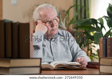 Old man in glasses reading a books in the room. Close portrait