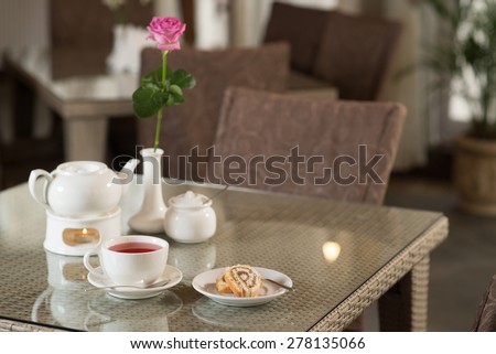 Cup of red tea, cake and rose on a table in a coffee shop
