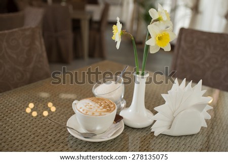 cup of cappuccino and a vase of beautiful flowers on the table