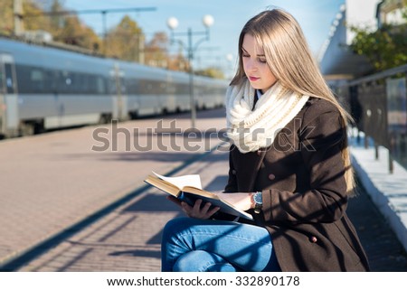 Young pretty woman reading a book on the train station in sunny day