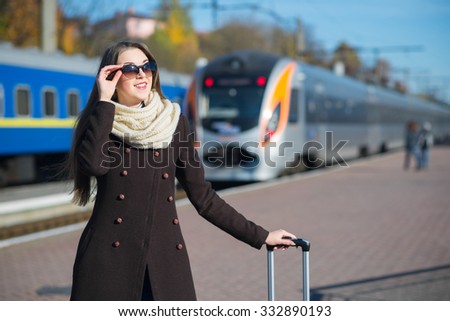 Young pretty woman with a suitcase on the train station in sunny day