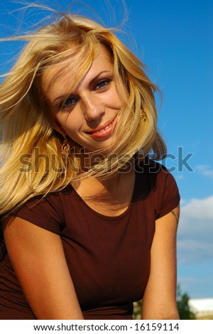 Smiling blond woman with fly-away hair against blue sky