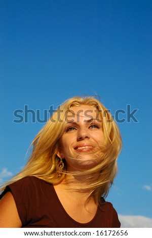 Smiling blond woman with fly-away hair against blue sky