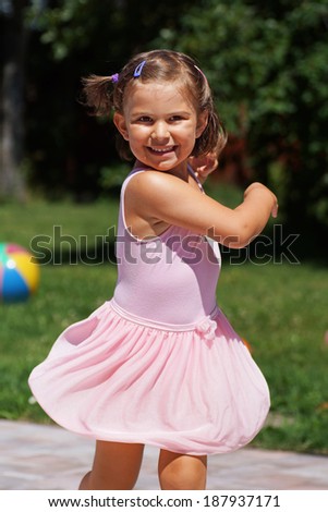 Cute and happy little girl dancing in pink ballet dress outdoor