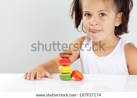 Cute little girl licking her lips in front of colorful stack of macaroons
