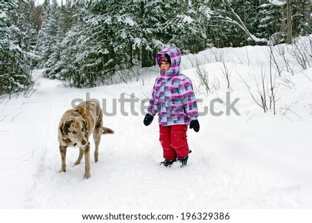 Little girl walking in the snow and the woods with her big dog