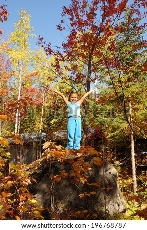 Little girl on top of big rock during fall in the colorful forest, playing king of the world,