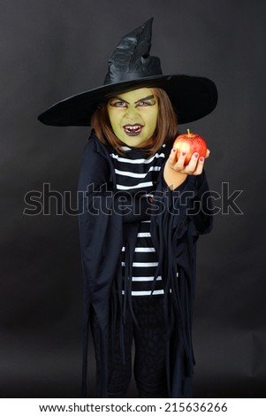Wicked witch offering poisoned apple, kid in Halloween costume