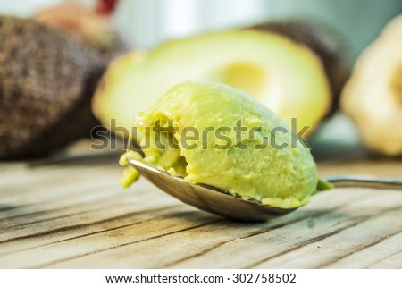 Green avocado on a spoon, in front of avocados and garlic