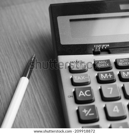 Calculator and pen on the table in back and white color.
