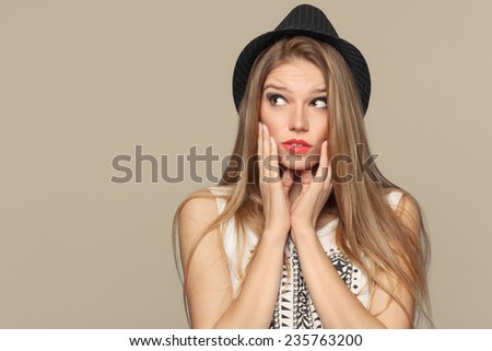 Surprised happy beautiful young woman looking up in excitement. Fashion girl in hat. isolated on beige background