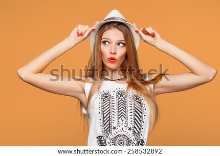 Surprised happy young woman looking sideways in excitement. Isolated over orange background