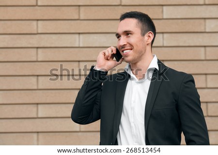 Smiling happy man talking on mobile phone in a black suit, happy modern man. Outdoors