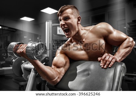 Muscular man working out in gym doing exercises with dumbbell at biceps, strong male naked torso abs