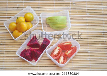 Four tropical fruits such as tomato, apple, orange and dragon fruit on separate plastic box with top shot mode