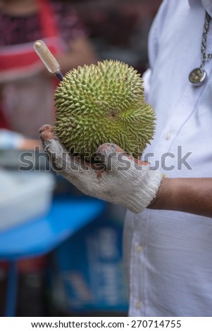 Merchant is evaluating the condition of the durians by using a wooden stick to knock on the durians peel.