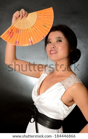 Asian female model wearing white dress. Young Chinese girl holding fan in hand, smiling gently.