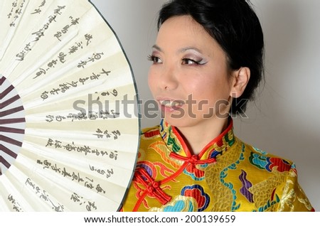 Elegant Chinese lady wearing traditional colorful dress. Kind female model from Asia holding fan in her hand.