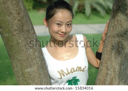Chinese girl in park. Standing between trees, relaxing with kind smile, wearing traditional Chinese dress.