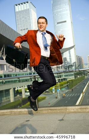 Happy, successful businessman - jumping. Wearing red suit and blue tie. Modern skyscrapers as background.