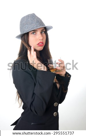 Young female model holds cigar and glass of whiksy. Girl puts black tail-coat and grey hat.