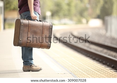 Casual traveler tourist legs waiting in a train station with a retro suitcase