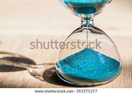 Sand running through the bulbs of an hourglass measuring the passing time in a countdown to a deadline, on a bright wooden background with copy space.