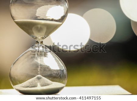 Modern Hourglass -- sand trickling through the bulbs of a crystal sand glass on bokeh background. every second counts. symbol of time. countdown. sandglass.