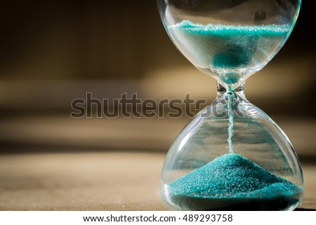 Sand running through the bulbs of an hourglass measuring the passing time in a countdown to a deadline, on a dark background with copy space.
