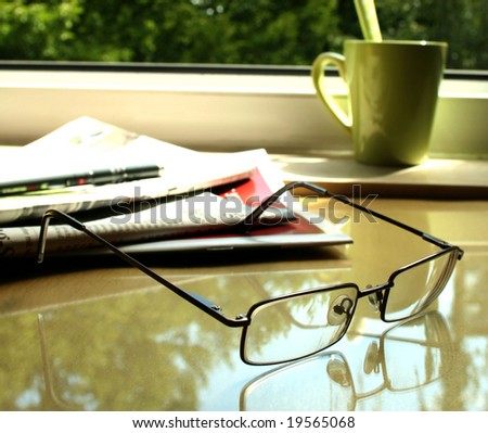 eyeglasses, newspaper on table and green cup