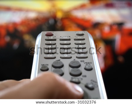 closeup of a hand  holding the remote control in front of the television, shallow DOF, conceptual image of the world under control