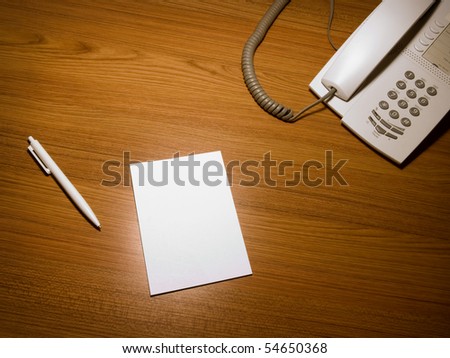 Blank white paper on the wooden working desk with the pen and telephone,shot taken from above