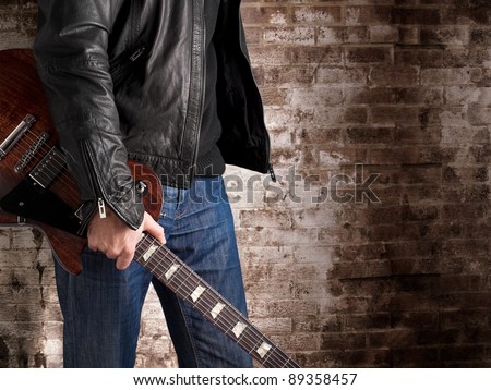 Man in a leather jacket standing in front of the brick wall and holding electric guitar,for music,concert,entertainment, themes
