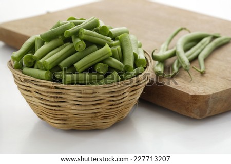 Raw cut french beans in cane container along with chopping board on white background