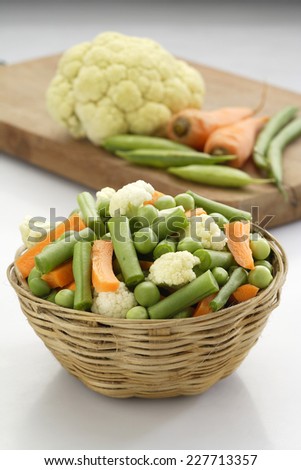 Raw cut mix vegetables in cane container along with chopping board, Carrot, Cauliflower, French beans, Green Peas