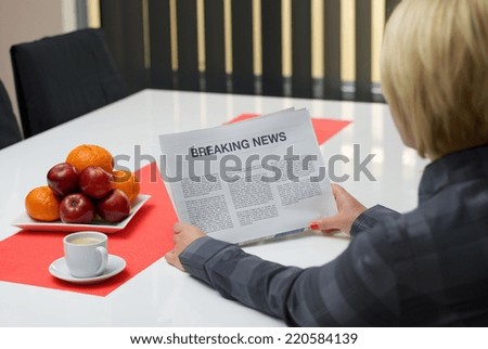 Woman reading breaking news article in the newspaper at home.