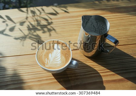 latte art coffee with milk pitcher on wood table