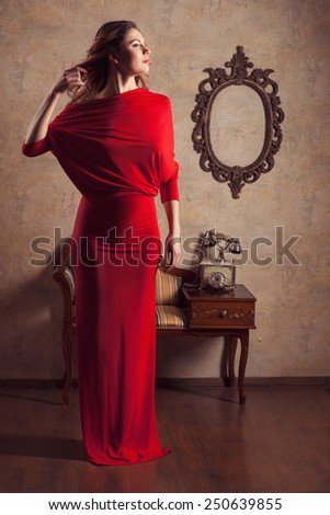 Beautiful girl in red dress looking away and straightens hair with her hand