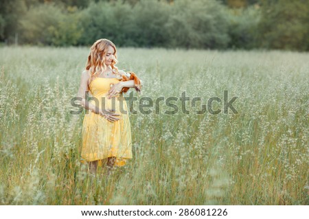Red-haired pregnant girl in a yellow dress standing in a field and rocks to sleep in the hands of a toy-rabbit