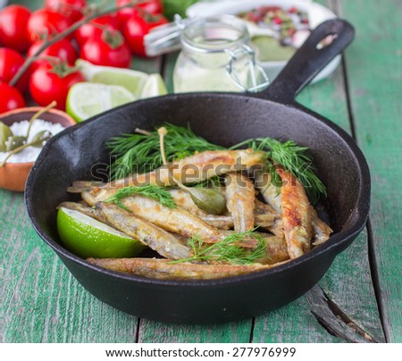 Fried smelt in the pan on the table with a sauce, lime, tomatoes, dill and garlic. Fried small fish.