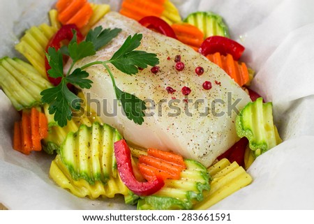 A piece of fresh fish fillets with spices and vegetables - potatoes, carrots, zucchini and bell peppers in parchment. Healthy eating, diet